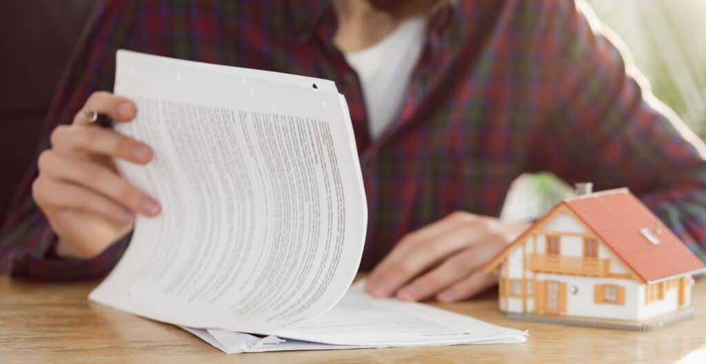 Should you do your own property tax protest or get help? A person looks over paperwork with a small house on the table representing the process.